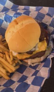 Cheeseburger with melted cheese on a soft bun, served with fries on a blue-and-white checkered liner.