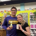 Two smiling friends pose in a bright shop, each holding ice cream cones and a cup.