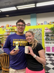 Two smiling friends pose in a bright shop, each holding ice cream cones and a cup.
