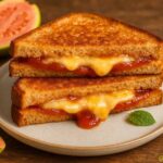 Two toasted bread slices with melty cheese and tomato jam filling on a plate, with fig halves in the background and a small mint leaf garnish.